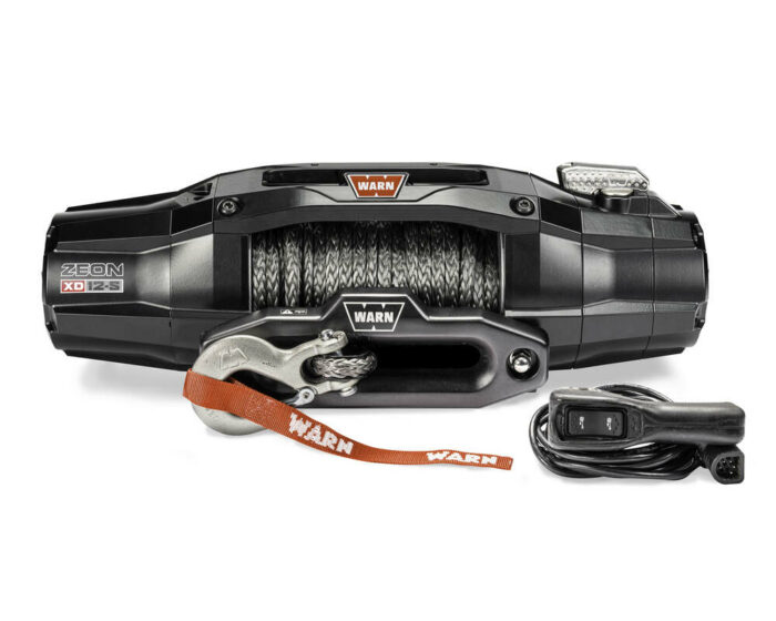 A Warn Zeon XD 12-S winch with a synthetic rope. The winch features a sleek black design with a visible hook and an orange strap branded "Warn." A handheld remote controller is placed nearby.